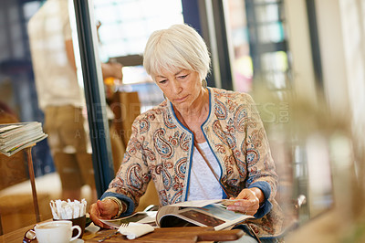 Buy stock photo Shot of a senior woman reading a magazine in a cafe