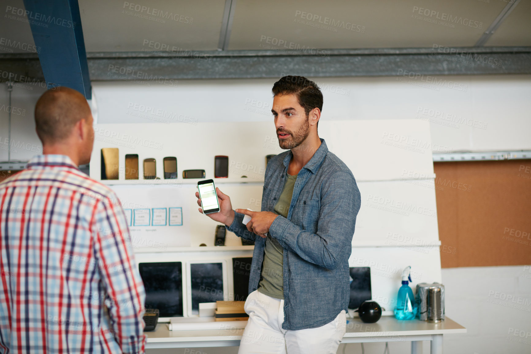 Buy stock photo Shot of a young man showing his coworker something on a mobile phone