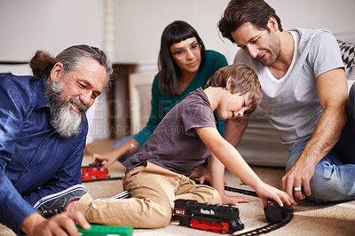 Buy stock photo Cropped shot of a young child playing with a train set while his family watches