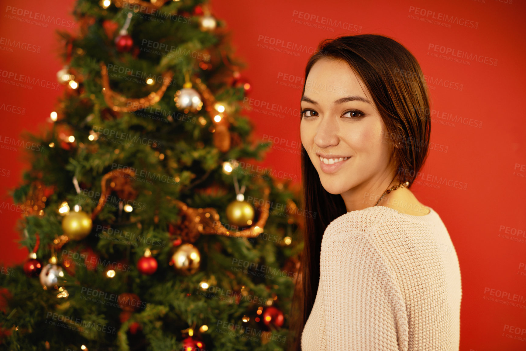 Buy stock photo Happy woman, portrait and celebration by christmas tree on red background and indoor for winter holiday. Young,  person or smile on face for xmas season for present or natural  pine with decoration