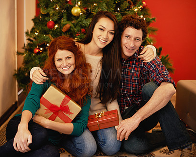 Buy stock photo Portrait of a group of young friends sitting by a Christmas tree holding their presents