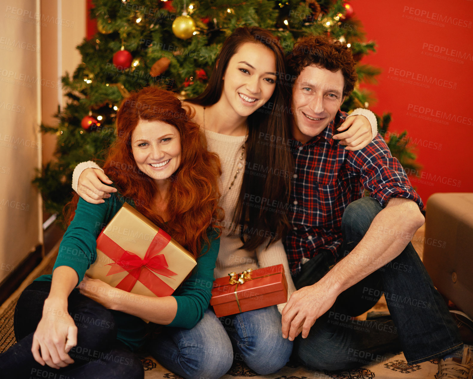 Buy stock photo Portrait of a group of young friends sitting by a Christmas tree holding their presents