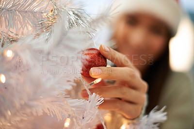 Buy stock photo Closeup of woman decorating a Christmas tree during the festive season. Female putting red baubles on a white tree with lights. Person decorating and preparing for the holidays in winter