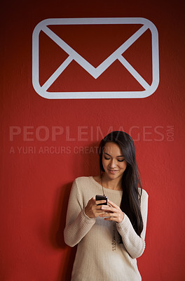 Buy stock photo Shot of a young woman sending a text message while standing in front of a red wall