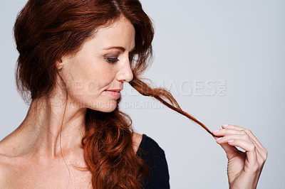 Buy stock photo Studio shot of a young woman holding her beautiful red hair against a gray background