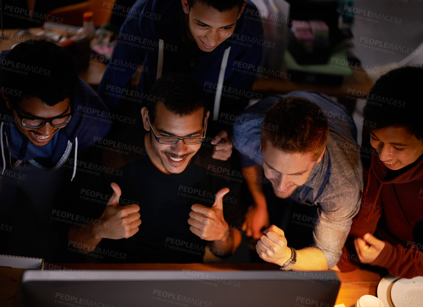 Buy stock photo Shot of a group of young man cheering at a monitor in a dark room