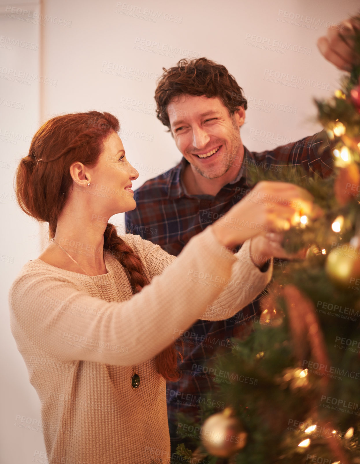 Buy stock photo Cropped shot of an affectionate young couple decorating the tree at Christmas