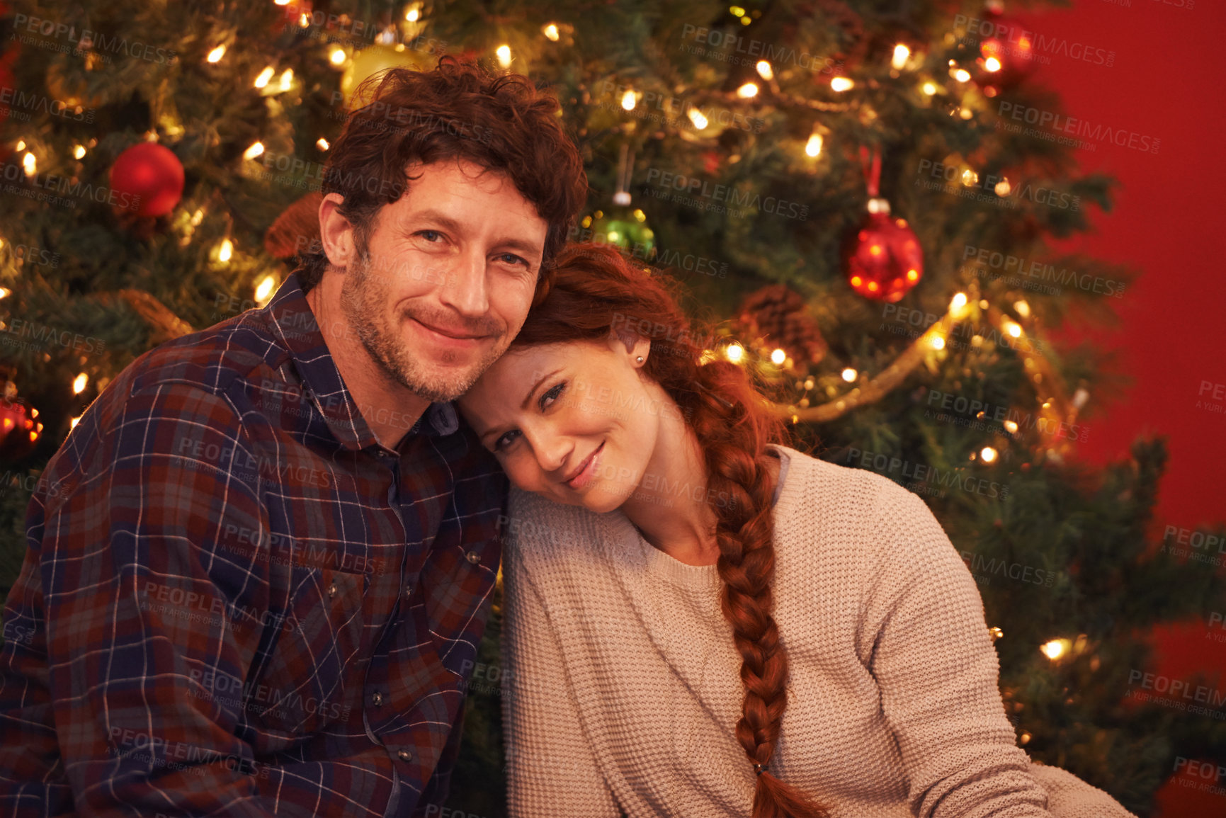 Buy stock photo Portrait of an affectionate young couple sitting by their Christmas tree