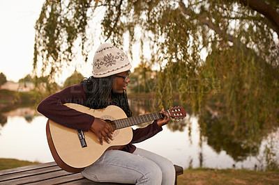 Buy stock photo Young woman, playing and guitar on bench by lake for music, passion and talent on string instrument. African lady, musician and composer of song in nature and jazz artist with practice for concert