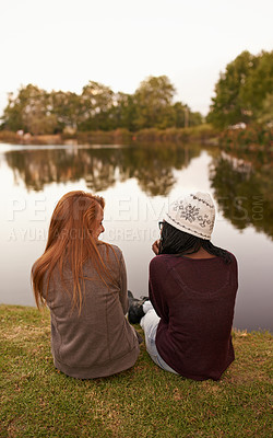 Buy stock photo Rear view shot of two teenage girls sitting and chatting next to a lake