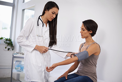 Buy stock photo Shot of a young woman getting her blood pressure tested by a doctor