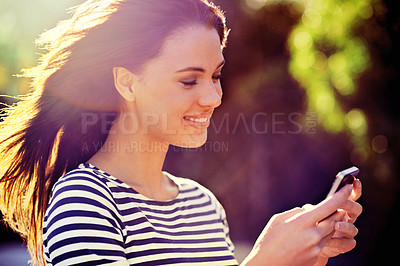 Buy stock photo Shot of a beautiful young woman using a mobile phone in the outdoors