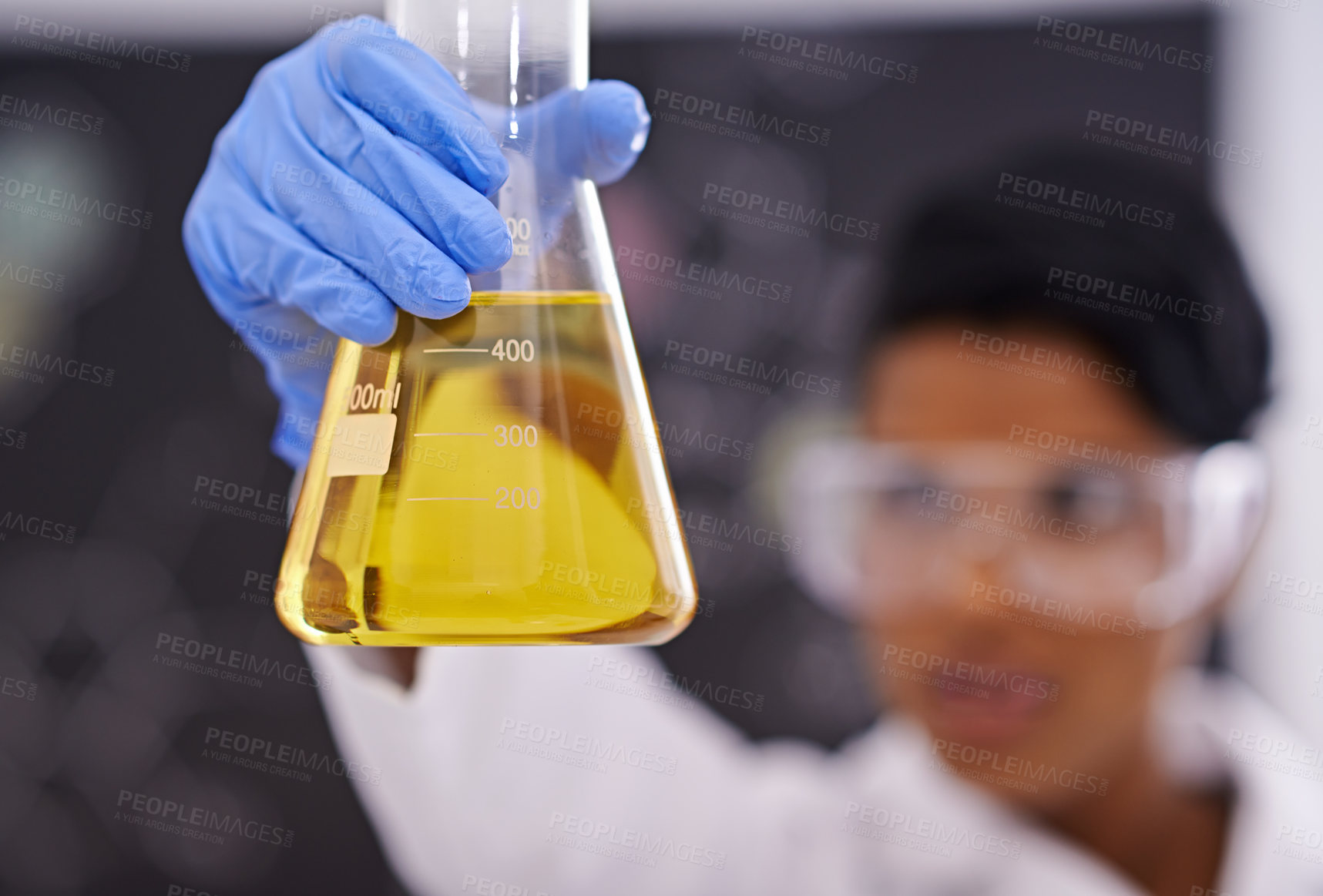 Buy stock photo A young scientist in protective clothing holding up a flask in her lab