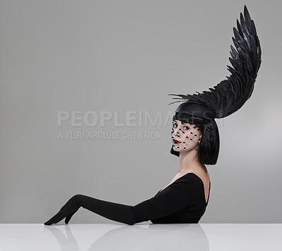 Buy stock photo Shot of a young woman in a wing-shaped headpiece sitting in a studio