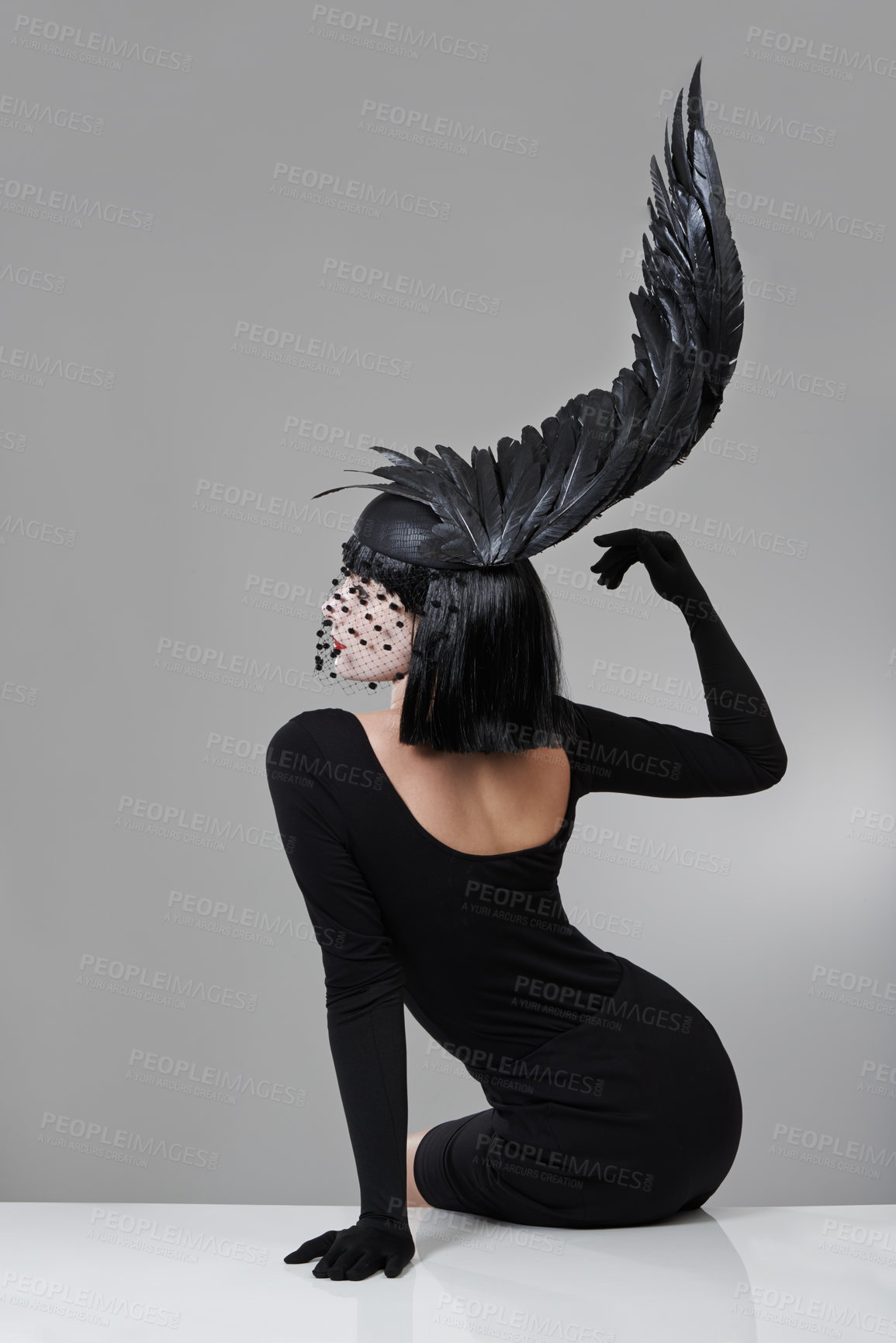 Buy stock photo Shot of a young woman in a wing-shaped headpiece sitting in a studio