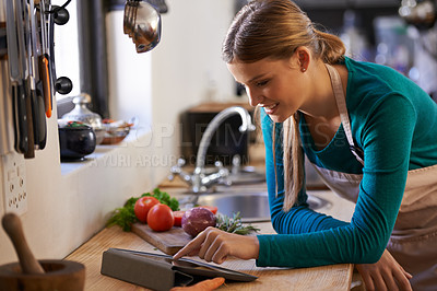 Buy stock photo Shot of a young woman looking at an online recipe on her digital tablet