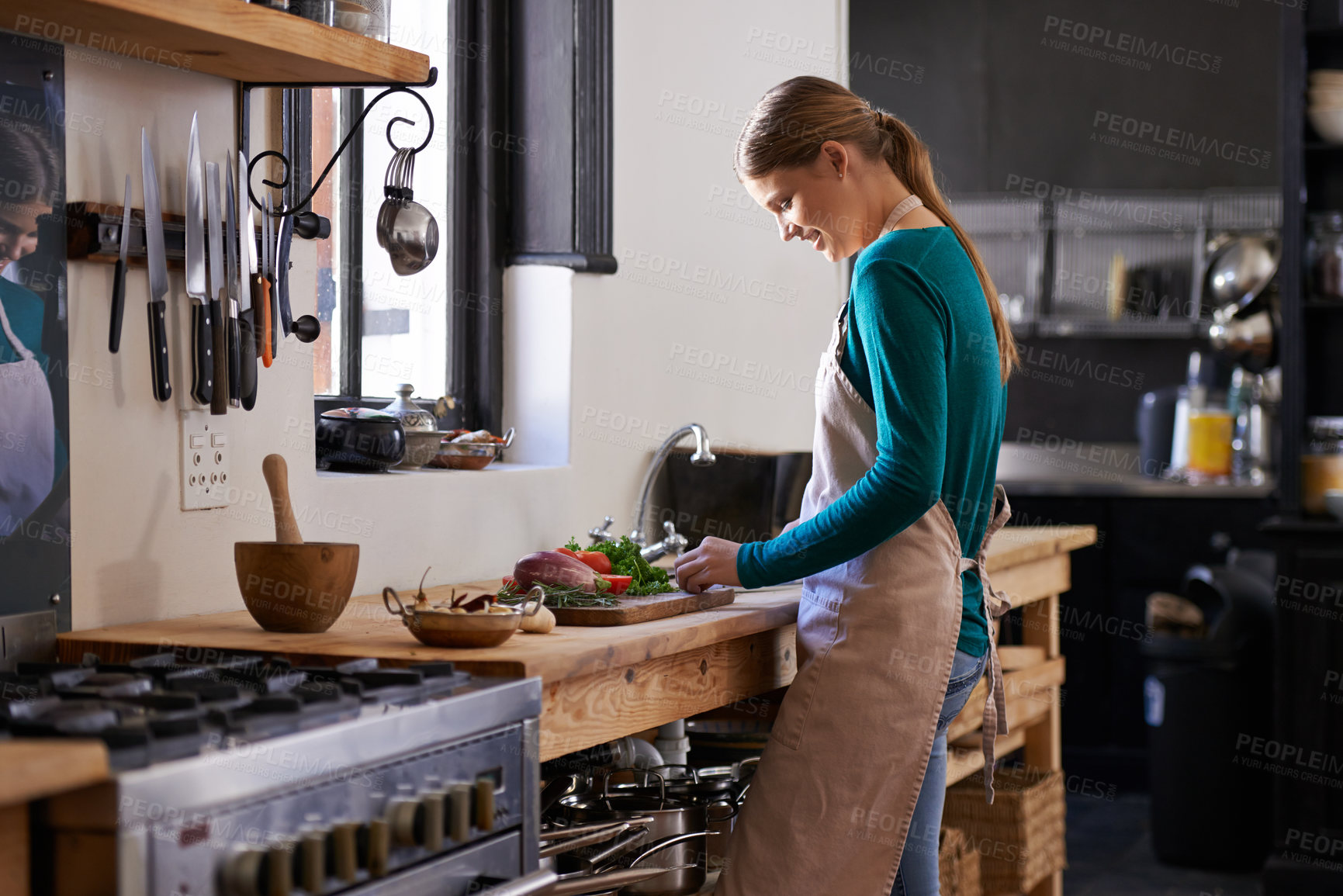 Buy stock photo Shot of a young woman chopping vegetables at a kitchen counter