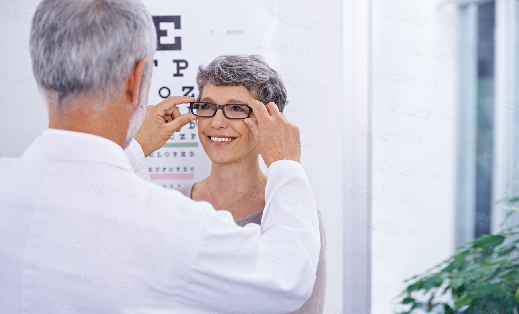 Buy stock photo Shot of an optometrist putting a pair of glasses on a patient
