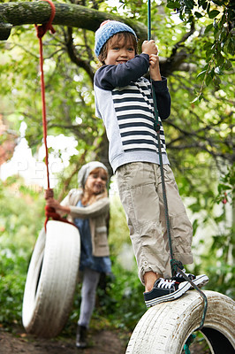 Buy stock photo Shot of two cute kids playing on tire swings in their garden