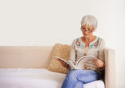 Buy stock photo Shot of a senior woman reading a book while sitting on a sofa