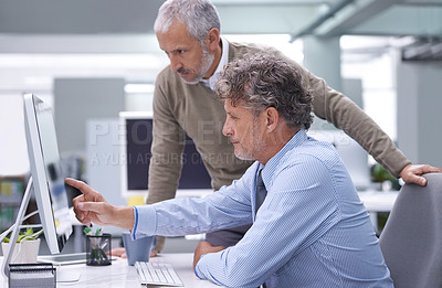 Buy stock photo A mature businessman sitting at his workstation explaining something to his colleague