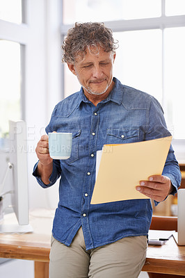 Buy stock photo Shot of a mature businessman having coffee  while looking through paperwork