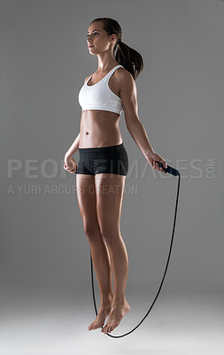 Buy stock photo Woman, fitness and jumping with rope in cardio workout, exercise or training on a gray studio background. Active female person or athlete skipping in balance, challenge or weight loss on mockup space