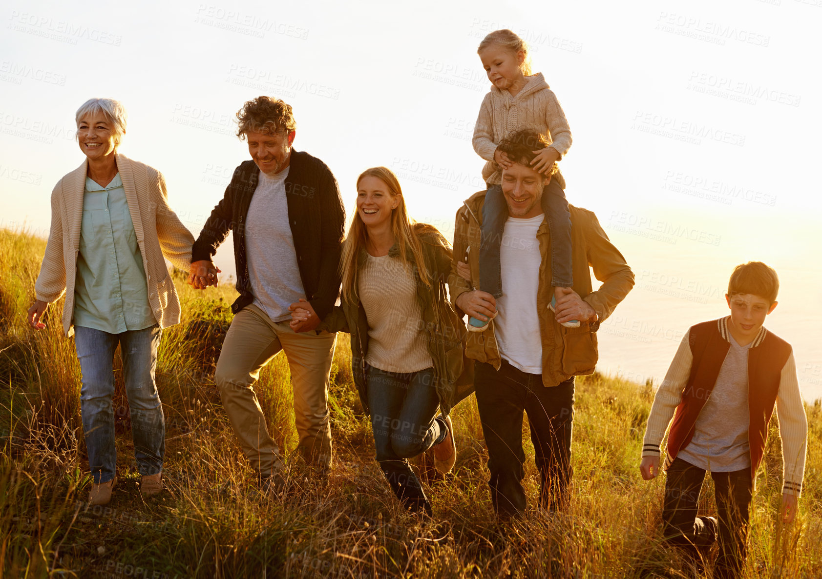 Buy stock photo A multi-generational family walking up a grassy hill together at sunset