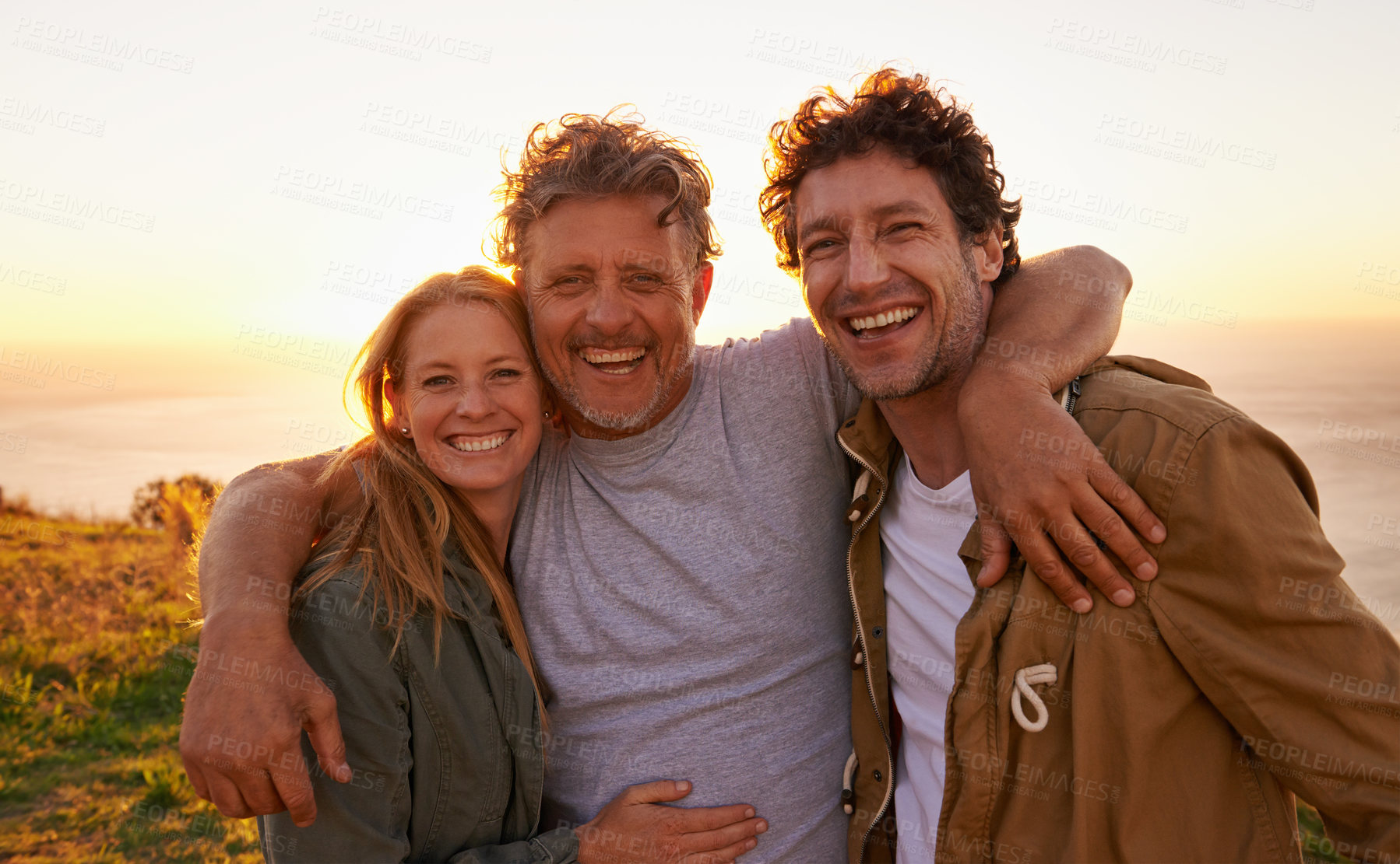 Buy stock photo Portrait of a father with his son and daughter on a grassy hill at sunset