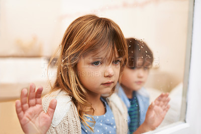 Buy stock photo Shot of two unhappy-looking young children looking out a window on a rainy day