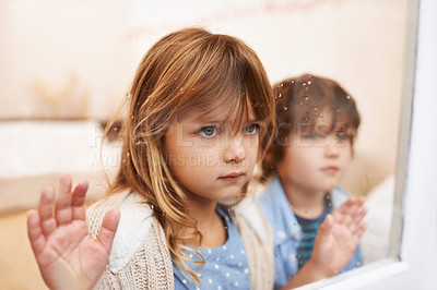 Buy stock photo Shot of two unhappy-looking young children looking out a window on a rainy day