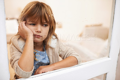 Buy stock photo Shot of a bored-looking little girl sitting and looking out a window on a rainy day