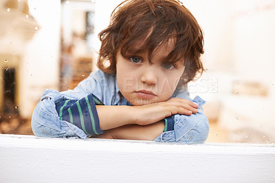Buy stock photo Portrait of an unhappy-looking little boy sitting and looking out a window on a rainy day