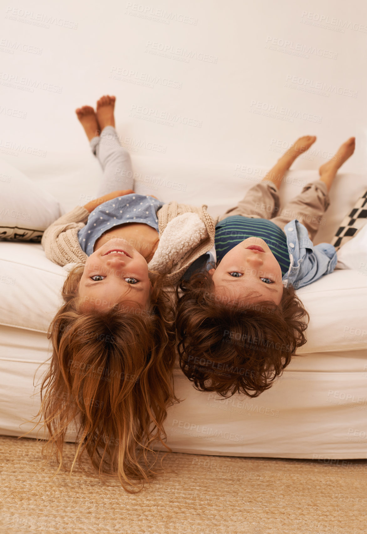 Buy stock photo Portrait of two young children lying on a sofa with their heads hanging over the edge