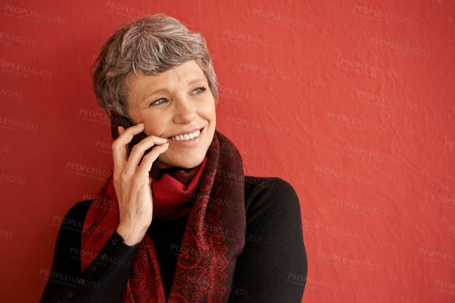 Buy stock photo Shot of a beautiful senior woman talking on her mobile phone in front of a red background