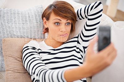 Buy stock photo Woman, selfie and funny or relax on sofa for silly communication and social media at home. Young person on couch in living room on mobile or internet for profile picture, tongue and face or emoji 