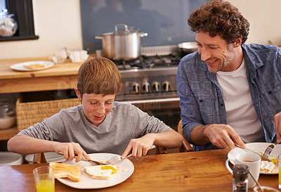 Buy stock photo A cropped shot of a young boy and his dad enjoying breakfast in their kitchen at home