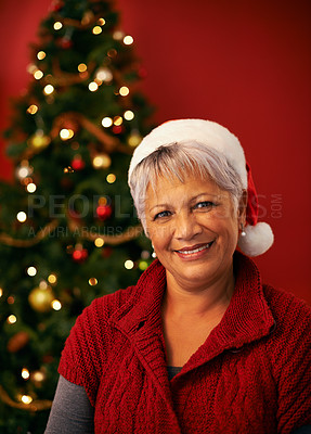 Buy stock photo Christmas, smile and portrait of senior woman in studio for holiday celebration by tree isolated on a red background. Xmas, mature and face of happy female person in hat for festive party in Brazil