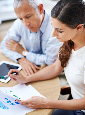 Buy stock photo Shot of two colleagues reading paperwork while sitting at a desk in an office