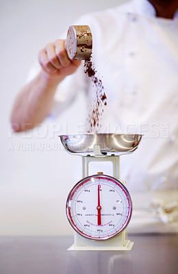 Buy stock photo Shot of a baker weighing a cup of cocoa powder on a scale