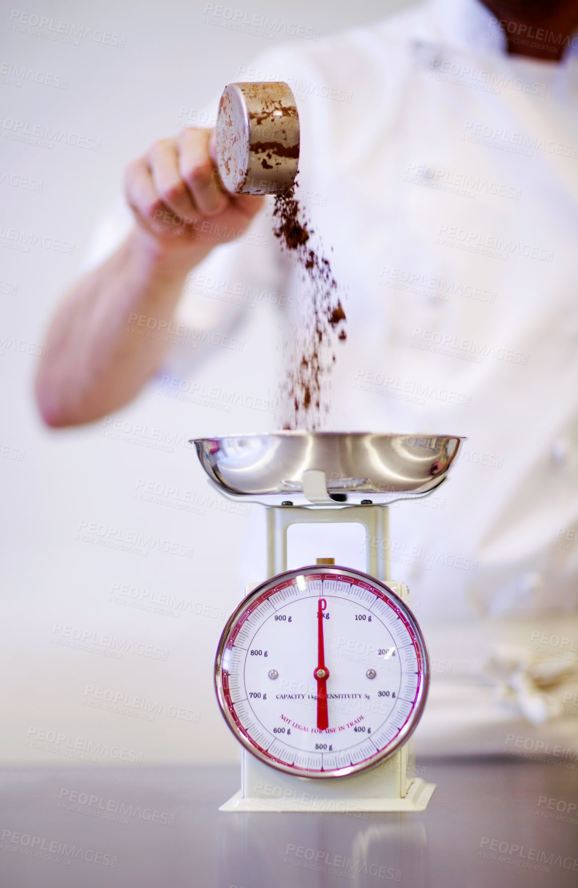 Buy stock photo Shot of a baker weighing a cup of cocoa powder on a scale