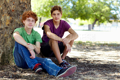 Buy stock photo Shot of two teenage boys relaxing in the shade of a tree at the park