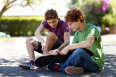 Buy stock photo Shot of two teenage boys working on their skateboards outside