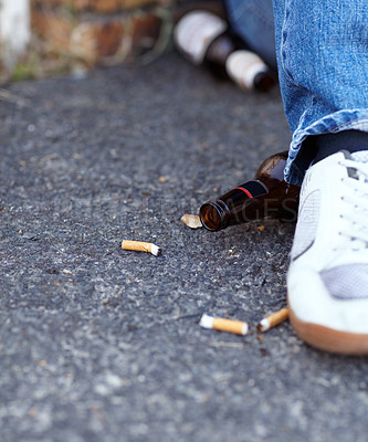 Buy stock photo Closeup shot of a person sitting next to discarded cigarette butts and beer bottles