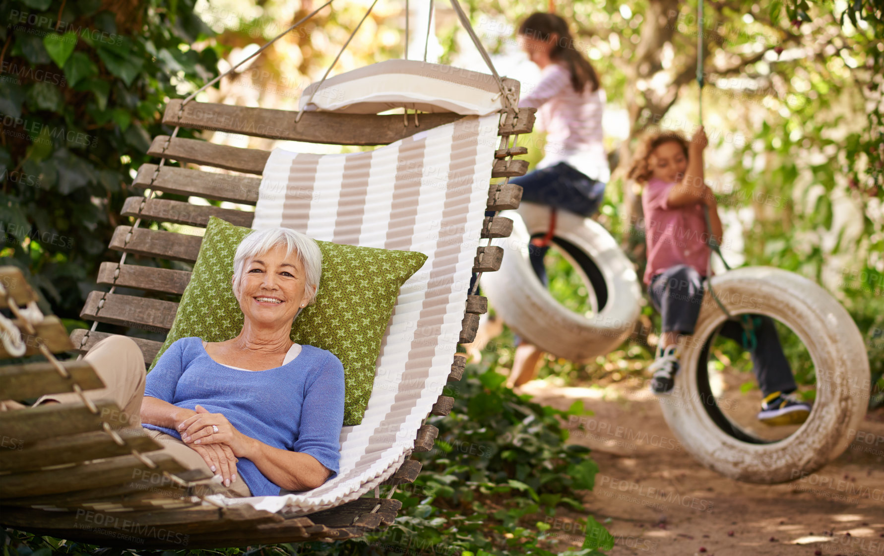 Buy stock photo Relax, happy and senior woman on a hammock while grandchildren play in the garden of the family home. Happiness, smile and portrait of elderly female person in retirement resting outdoor in backyard.