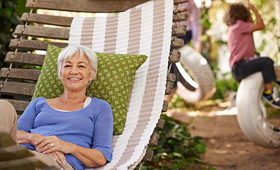 Buy stock photo Portrait of a senior woman lying in a hammock in the garden while her grandchildren play in the background