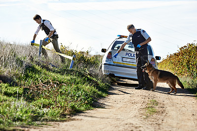 Buy stock photo Shot of two investigators erecting a barrier around a murder scene using police tape