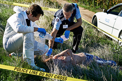 Buy stock photo Shot of two investigators examining the body at a crime scene