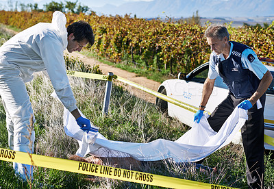 Buy stock photo Shot of two investigators placing a sheet over a dead body at a crime scene