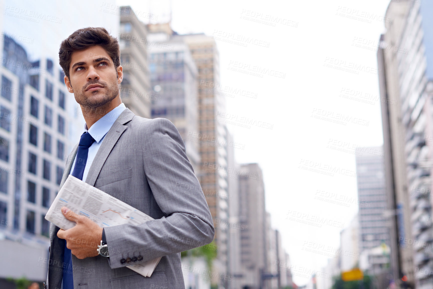 Buy stock photo A handsome young businessman with a newspaper walking in the city